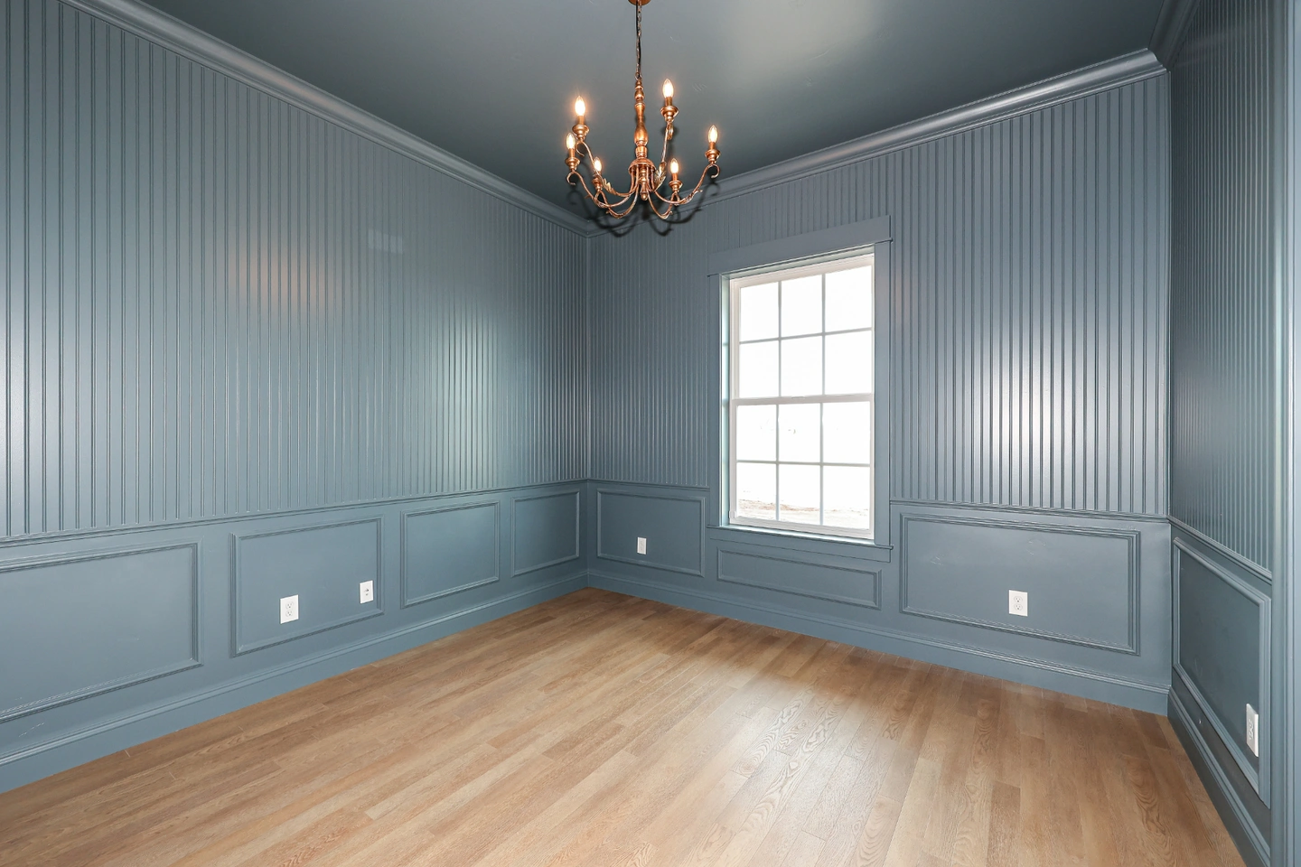 Empty room with blue wainscoting and beadboard walls, light hardwood floor, and a bright window.
